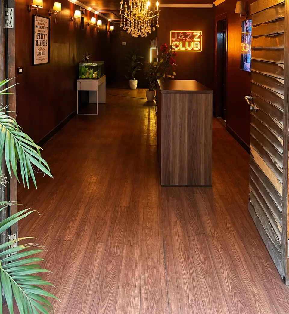 The Jazz Club entrance hall with a wooden floor, wall lamps, a chandelier and the reception desk