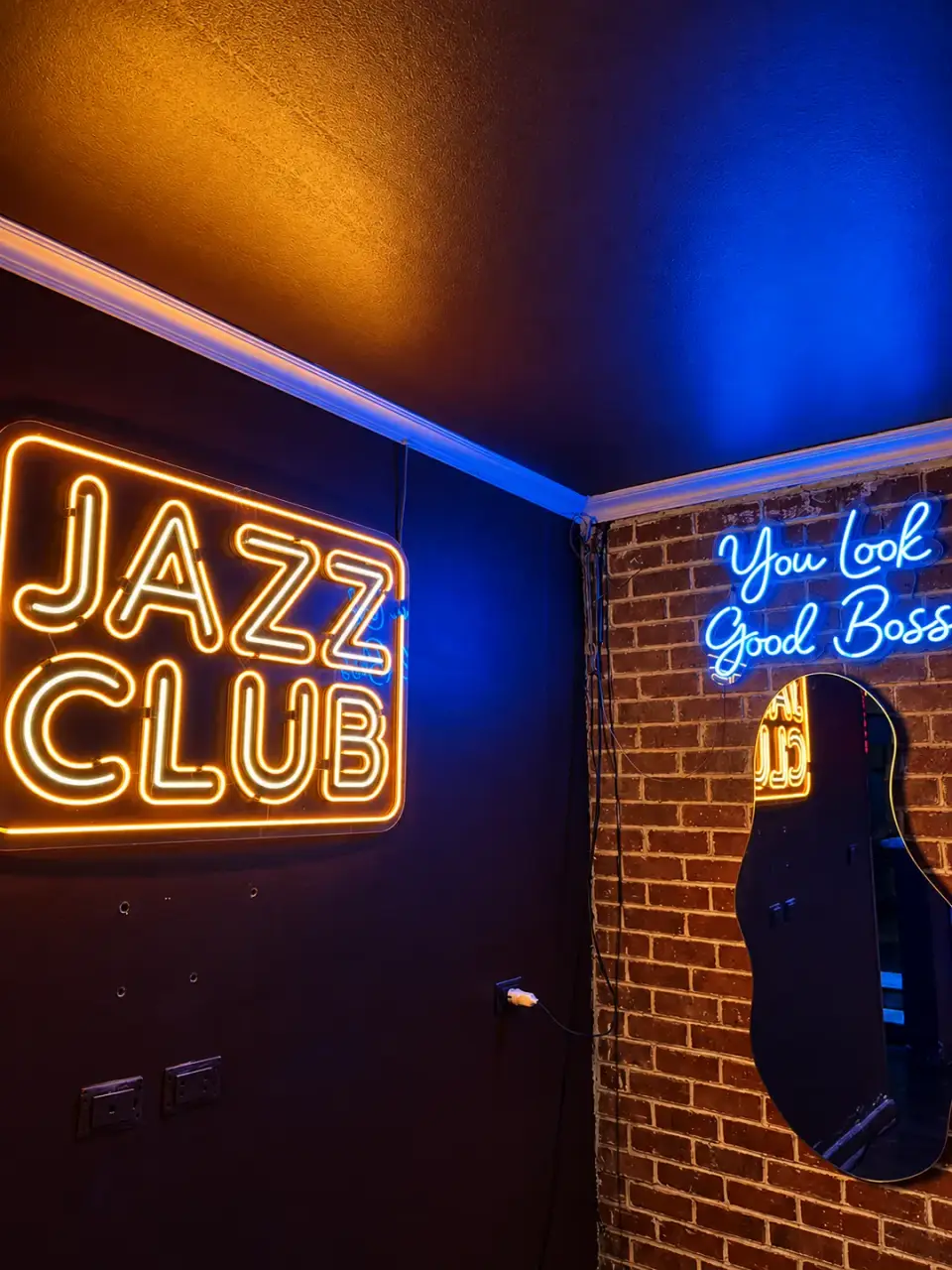 The JAZZ CLUB neon sign beside a blue You Look Good Boss sign on a brick wall
