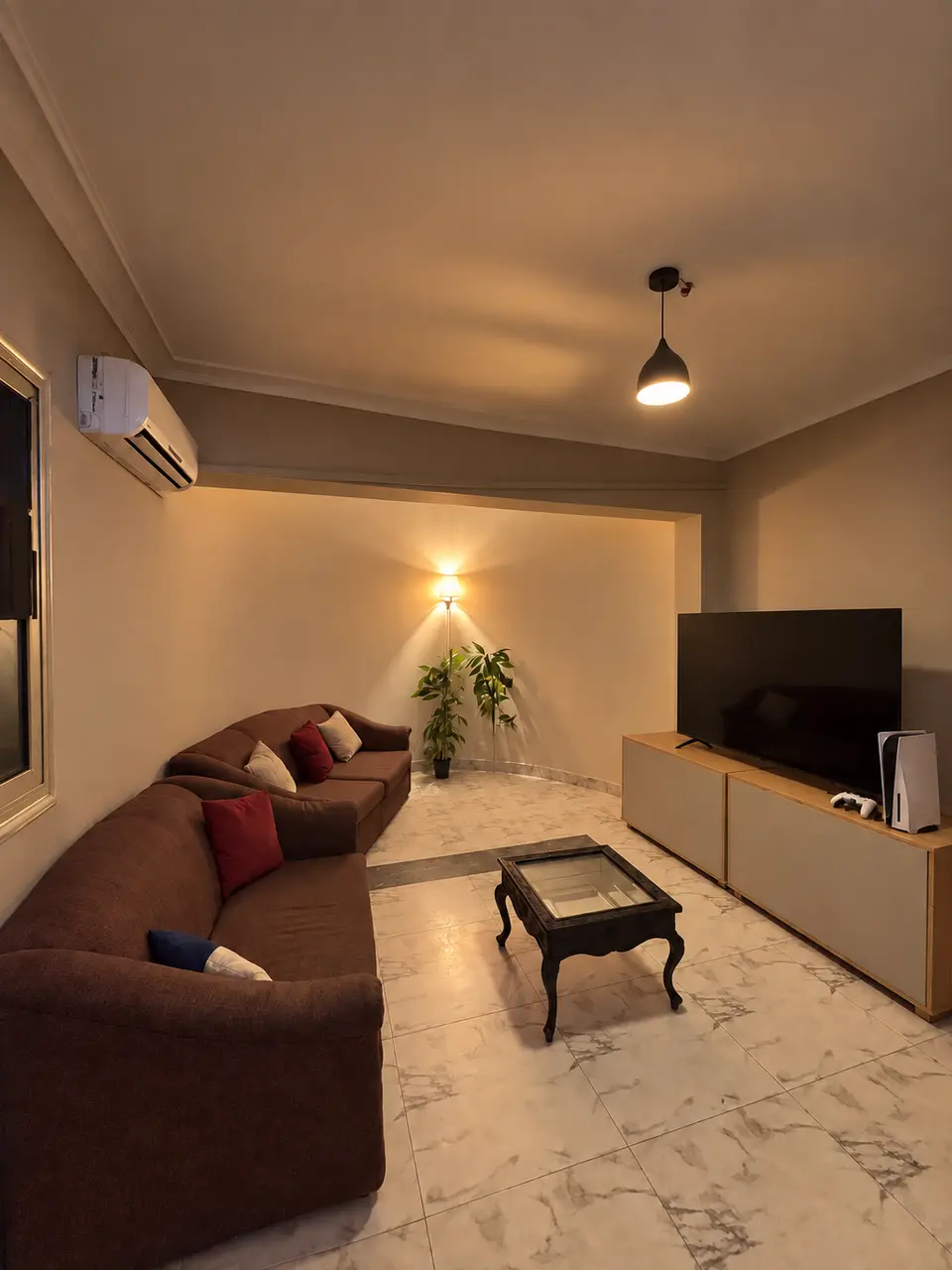 Room 03: brown sofa, glass coffee table, a plant and a TV with a PS5